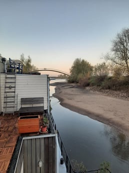 Uitzicht richting de Waal bij eb in de winter, met strand, passerende boten en wandelaars op loopbrug.